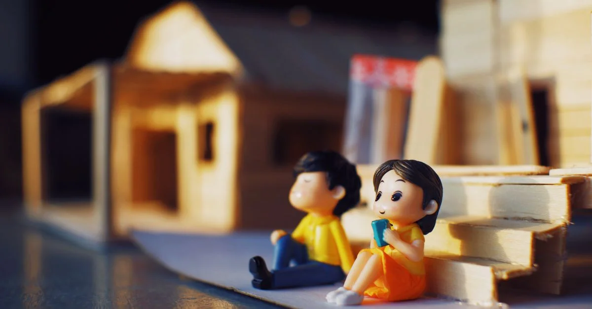 Adorables figurines de couple miniatures assises près d'une maison de poupée en bois.