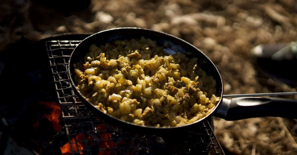 Poêle de pommes de terre grillées cuisinant sur un feu ouvert en extérieur. Repas rustique autour du feu de camp.