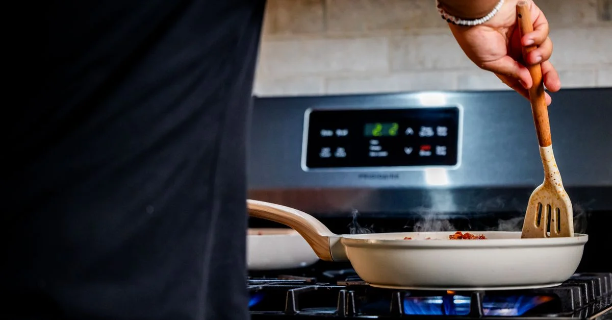 Personne cuisinant avec une poêle sur une cuisinière, montrant ses compétences culinaires à l'intérieur.