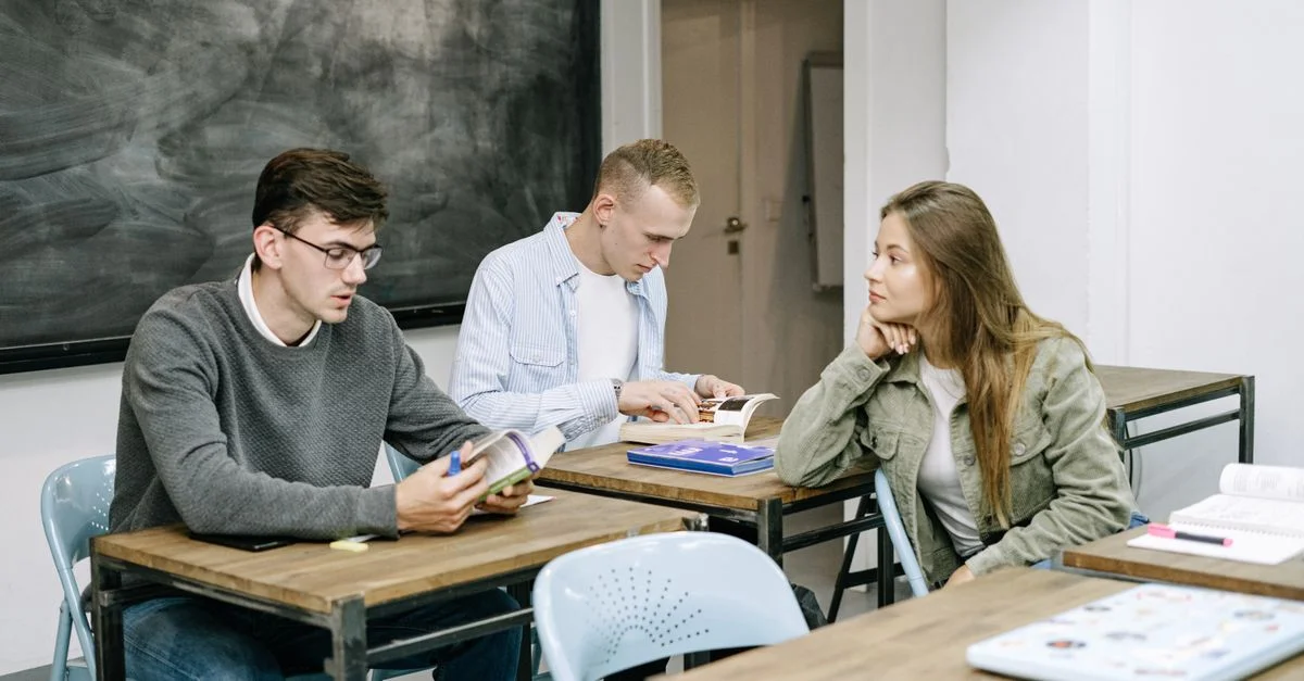 Groupe de jeunes adultes étudiant ensemble dans une salle de classe, engagés dans la lecture et la discussion.