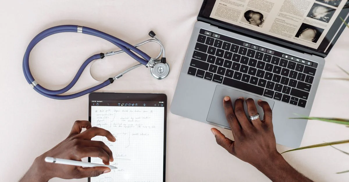 Professionnel de la santé utilisant une tablette et un ordinateur portable pour des recherches avec un stéthoscope sur le bureau.